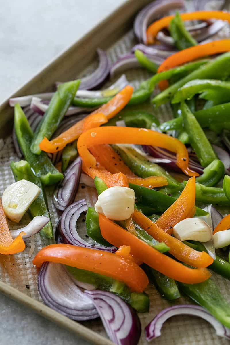 Sliced green and orange peppers with onions and garlic on a sheet pan tossed with olive oil