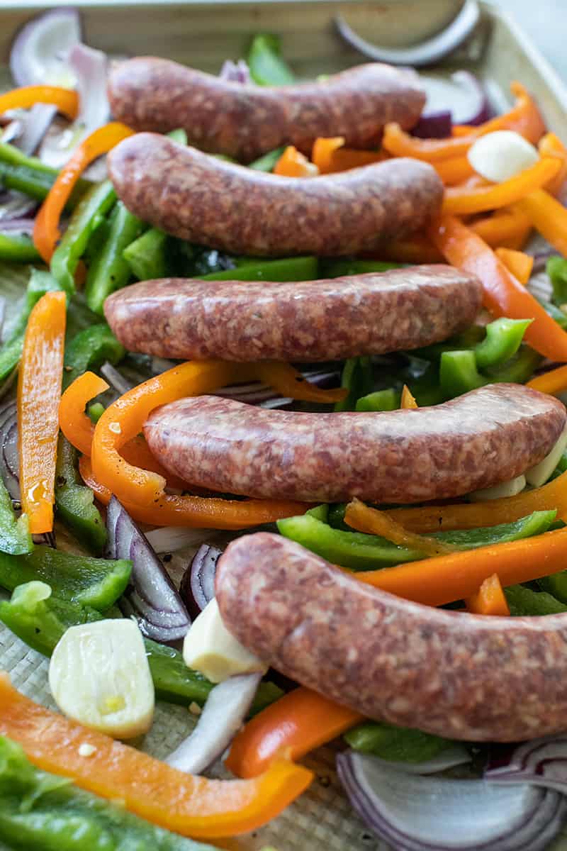 uncooked sausage on a bed of green and orange peppers.