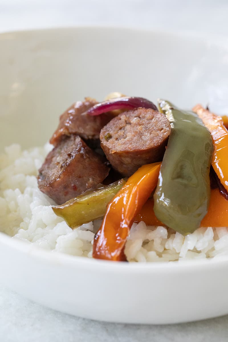 Sausage and peppers on white rice in a white bowl.