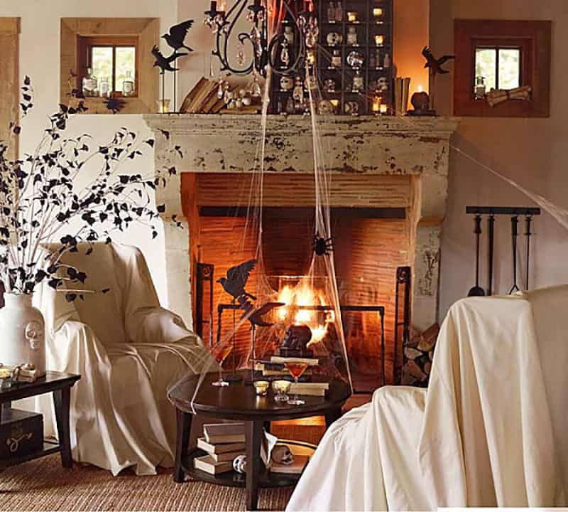 Spooky Halloween living room with sheets over the chairs, birds and bats and a lit fireplace.