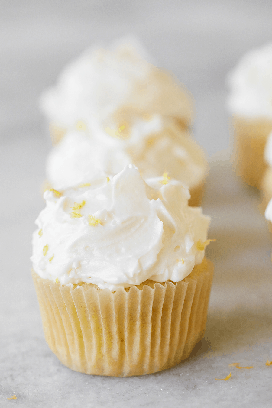 Lemon buttercream frosting recipe with lemon zest on the top of a vanilla cupcake.