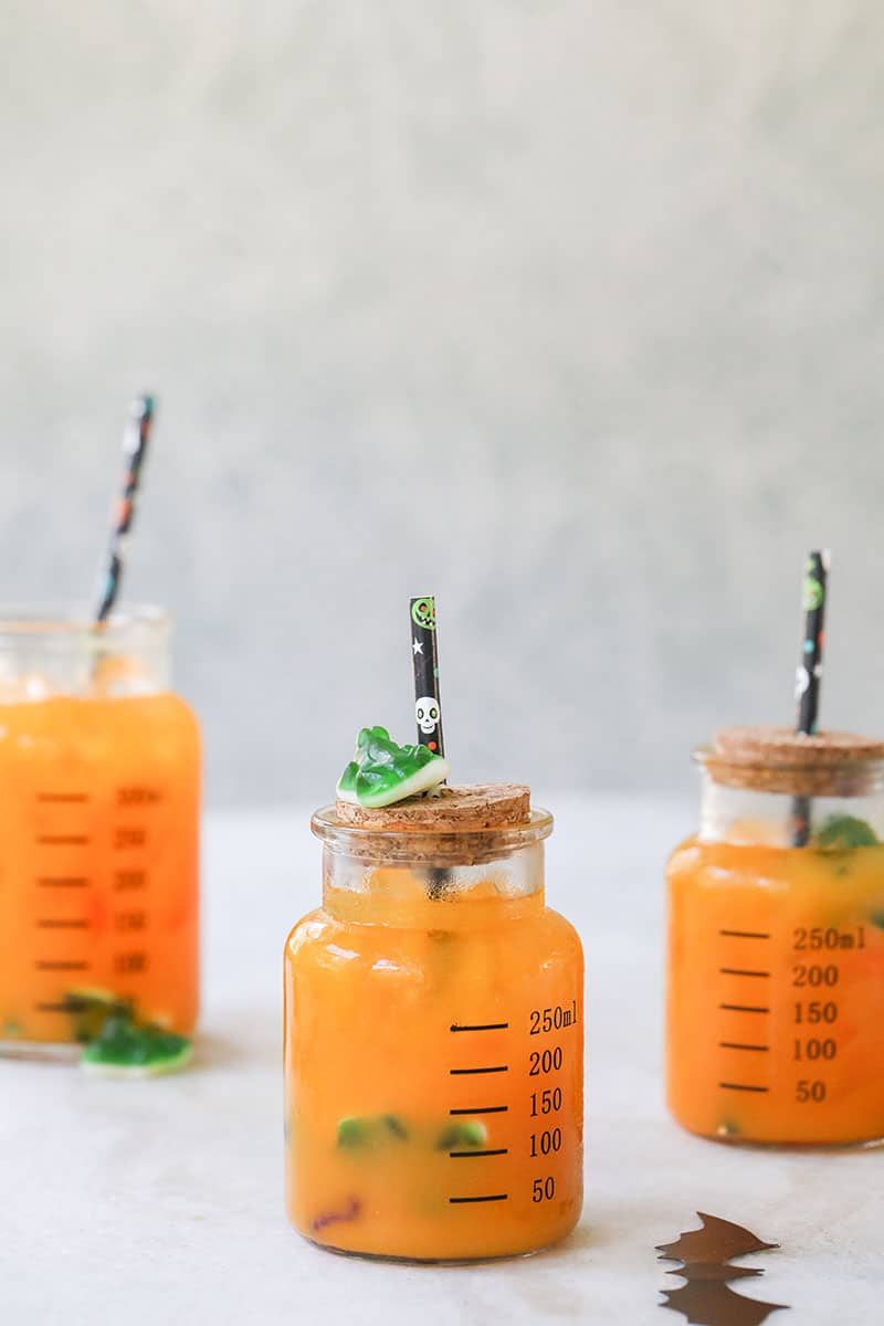 Bright orange Halloween punch for kids in a beaker with a Halloween straw.