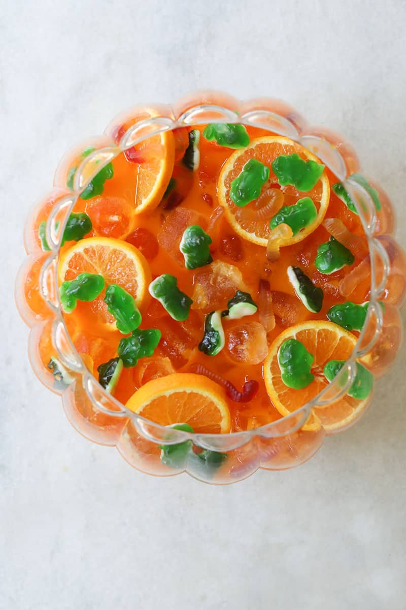 Overhead of an orange Halloween punch for kids with green frog mummies and gummy worms. 