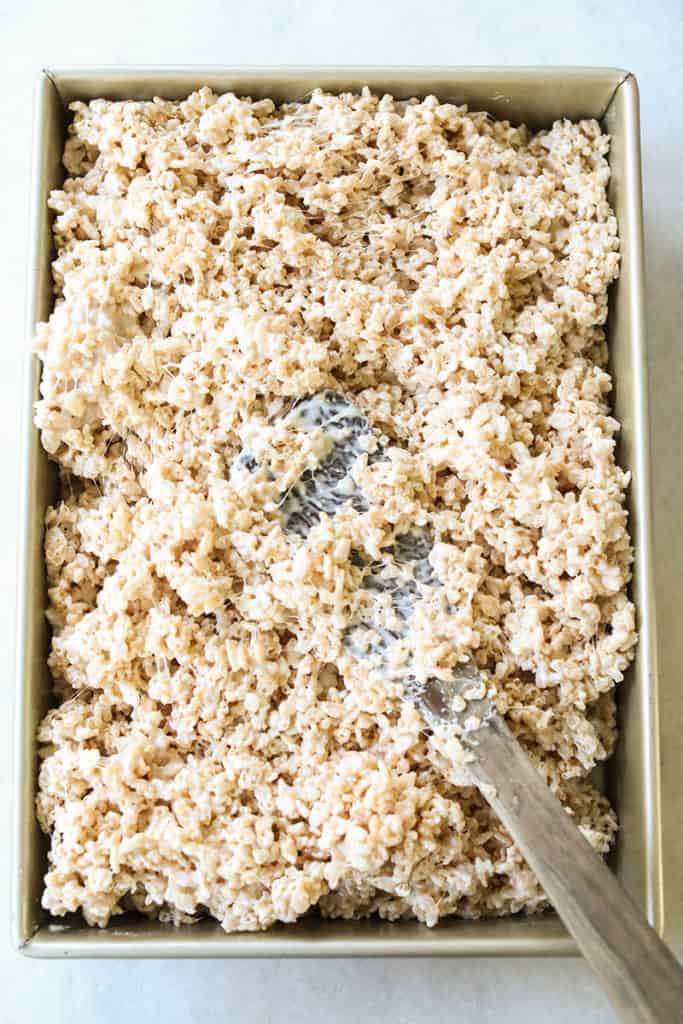 Pressing rice Krispie treats into a pan.