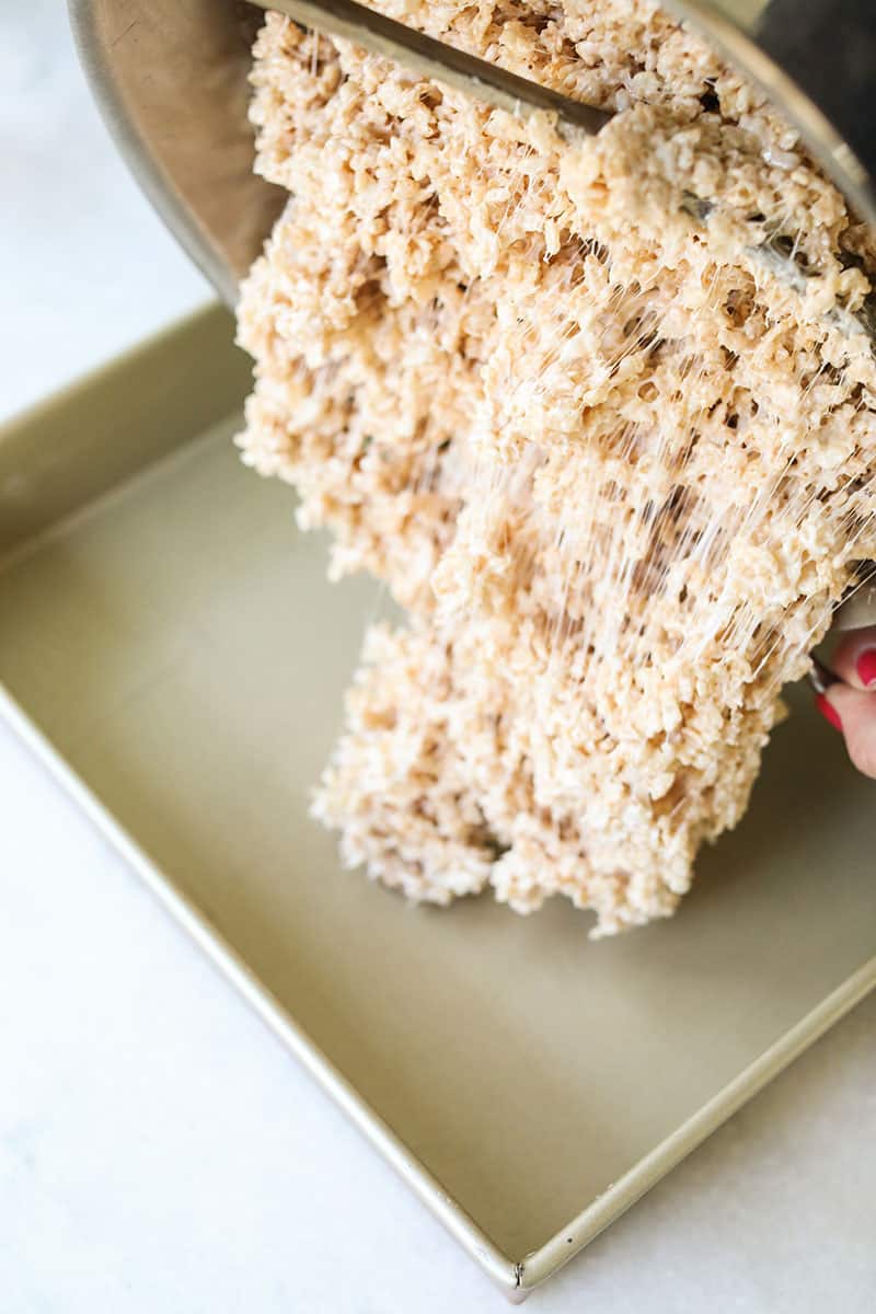 Rice Krispies being poured into a cake pan.