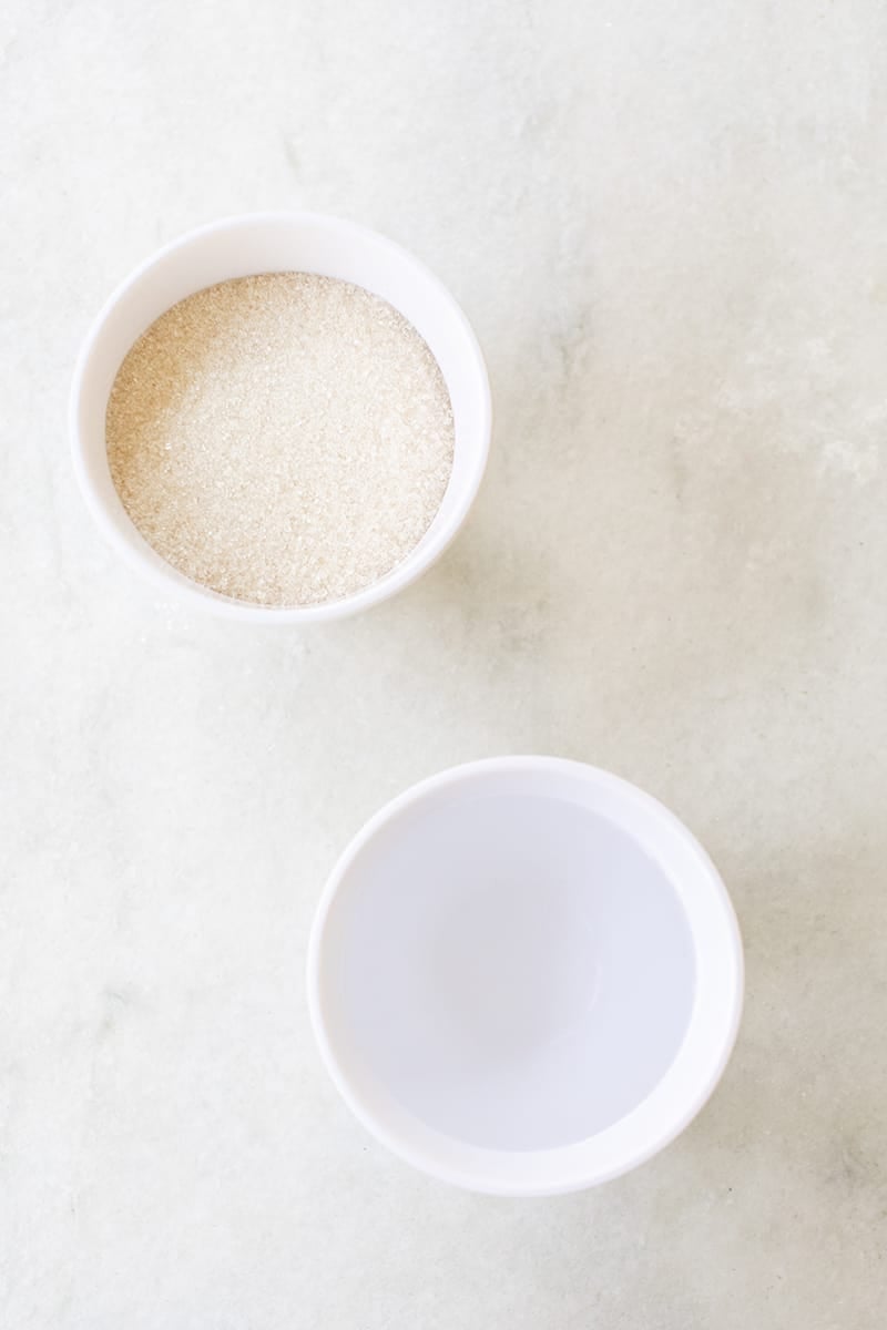 Bowl of water and a bowl of sugar on a marble table. 