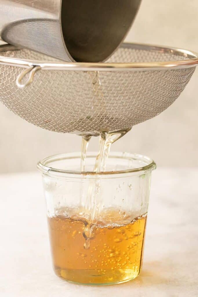 Pouring mint-infused simple syrup into a glass jar.