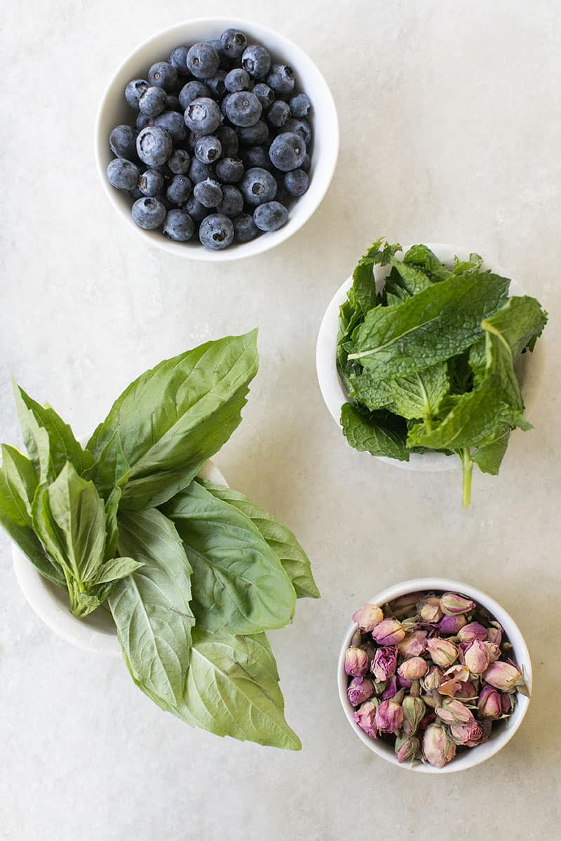 Herbs, dried rose petals and blueberries on a marble table. 