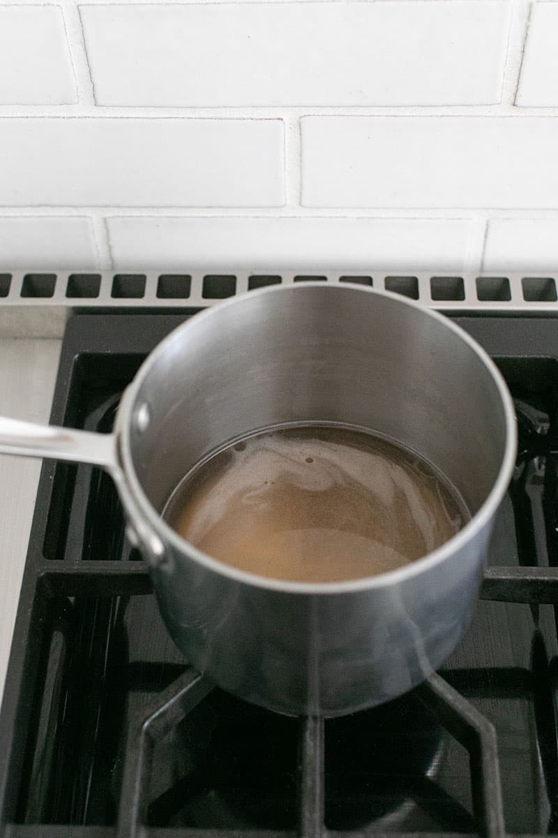 A saucepan on a stove with sugar melting inside. 