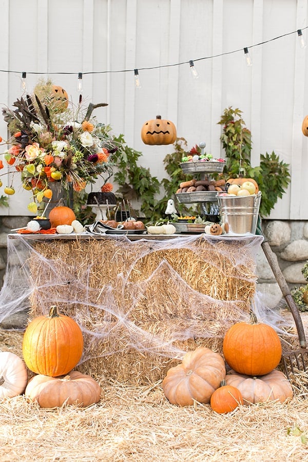 A Halloween party ideas set-up with hay stacks, tin buckets, pumpkins and string lights. 