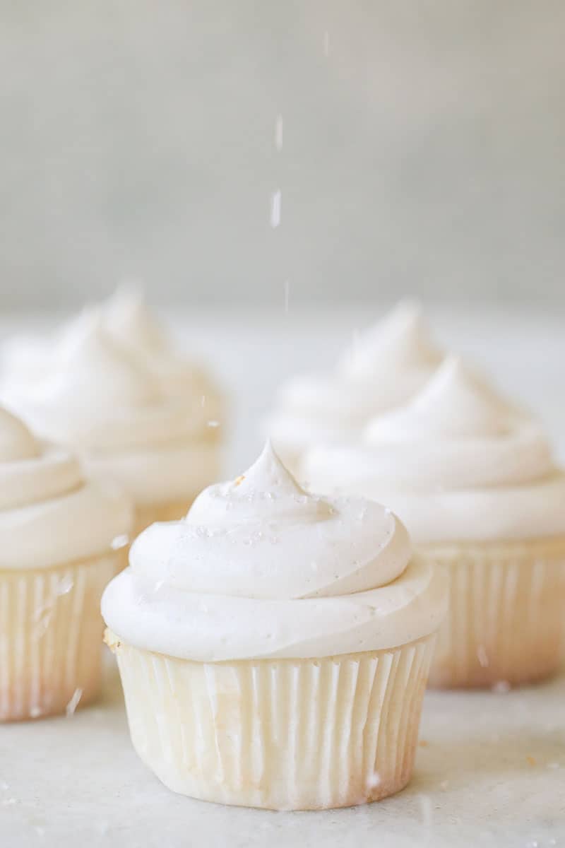 vanilla cupcake recipe with buttercream frosting and sprinkles being poured over the top.