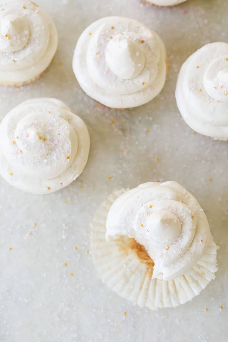 Five vanilla cupcakes overhead on a marble table with sprinkles.