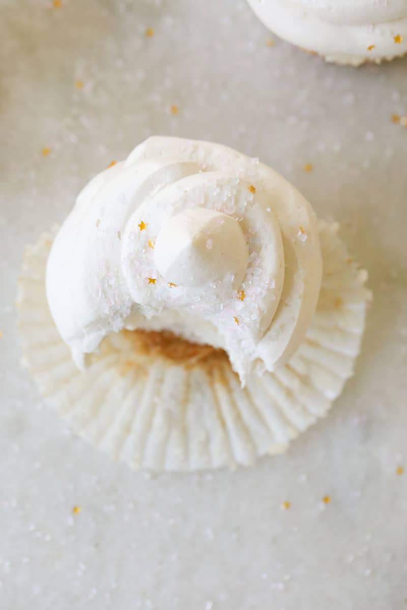 Overhead picture of a vanilla cupcake topped with buttercream and sprinkles with a bite taken out.