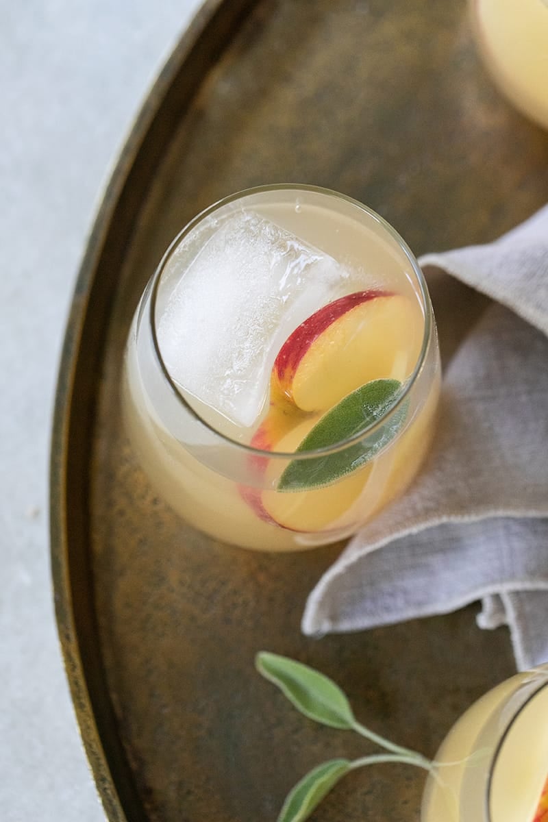 Wine spritzer with apple and ginger on a gold tray and a large ice cube. 