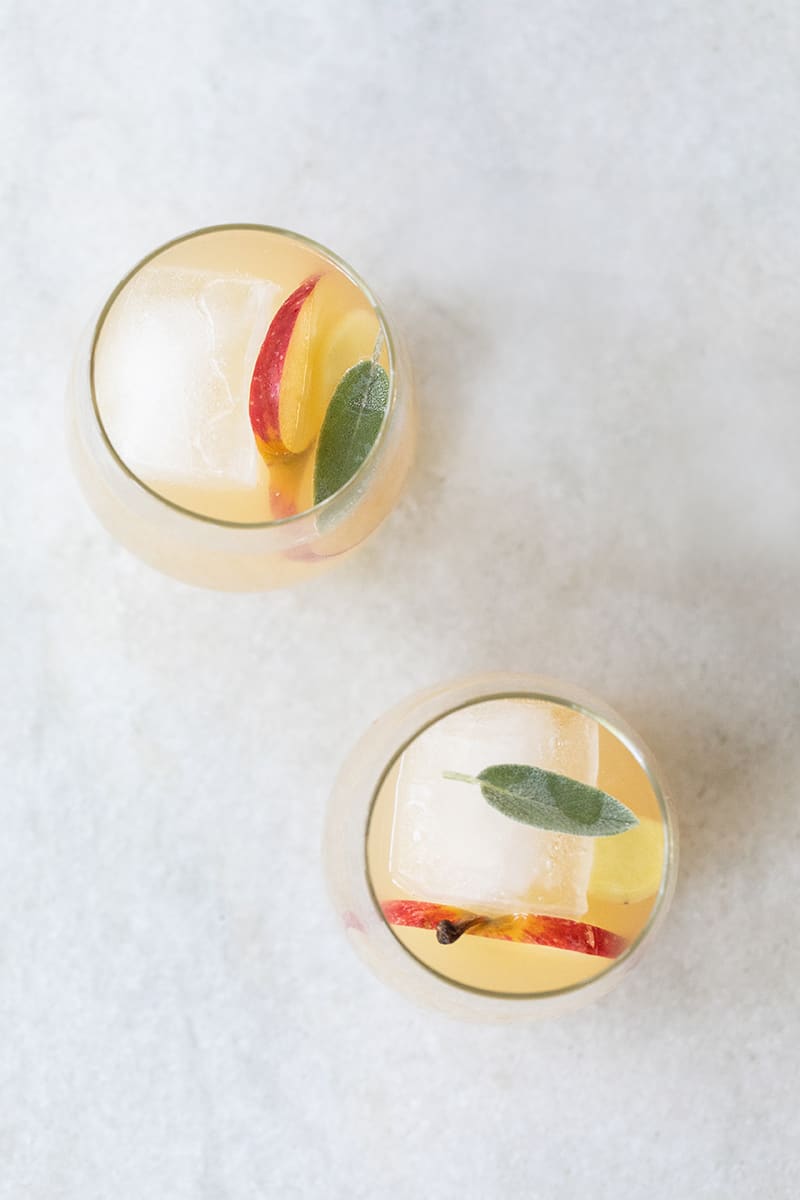 Fall wine spritzers on a marble table with apple, ginger, sage, white wine, Lillet. 