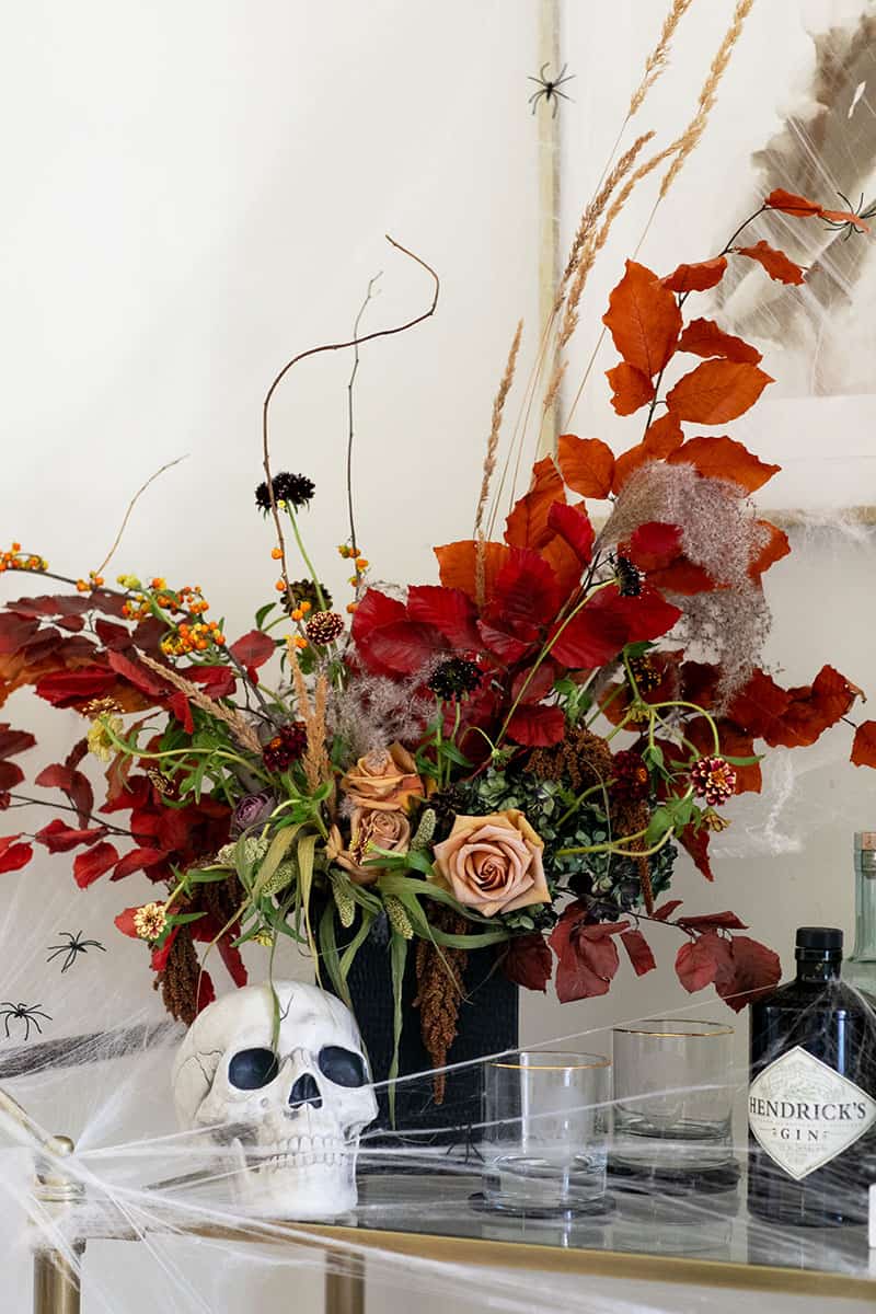 Beautiful Halloween flowers with skull and glasses on a bar cart for an inexpensive​ Halloween decorating idea., hot glue, halloween season, spray paint