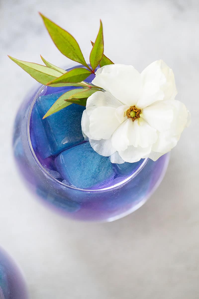 Mermaid inspired cocktail with blue ice cubes and a white flower. 