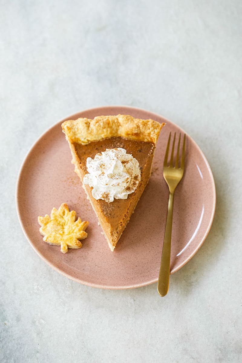 Slice of pie with whipped cream on a pink plate with a gold fork.