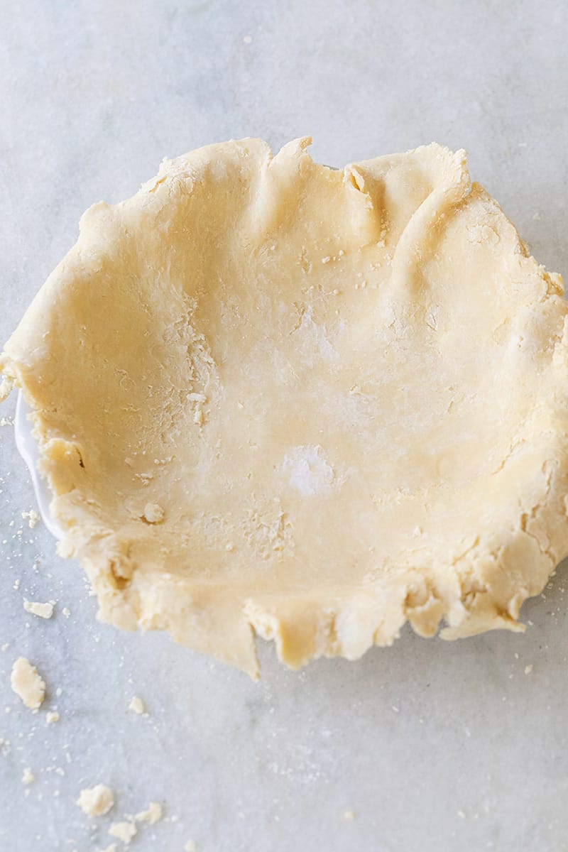 Pie crust rolled out and set on a pie dish about to be formed into pie crust.