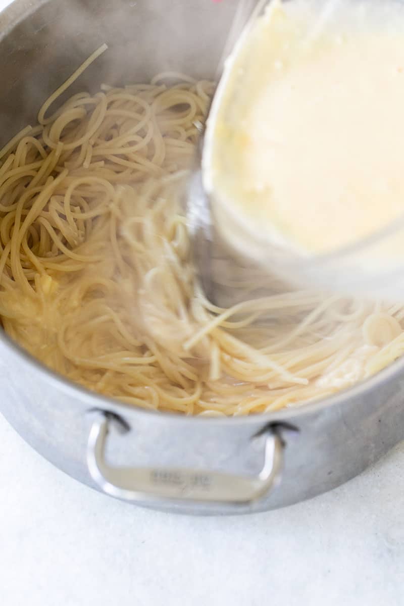 Carbonara sauce being poured into hot pasta.