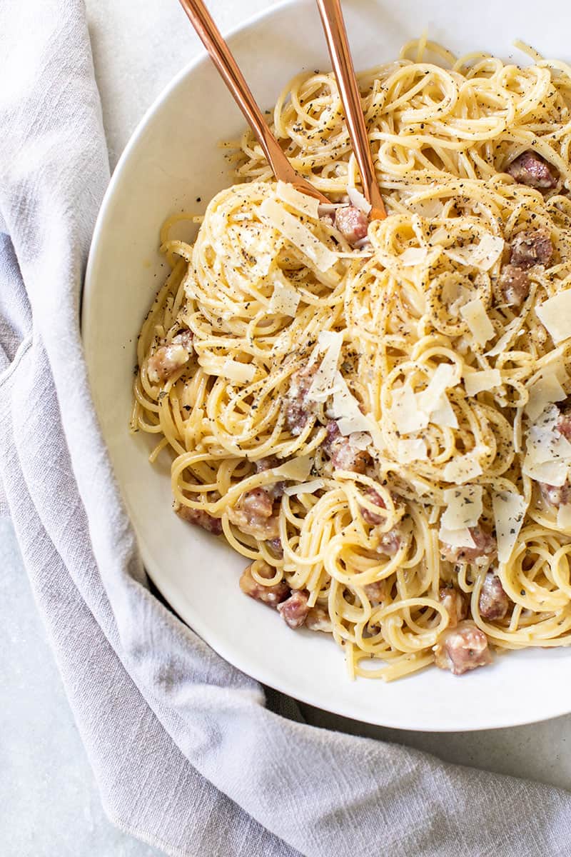 Pasta Carbonara in a white serving bowl with copper spoons.