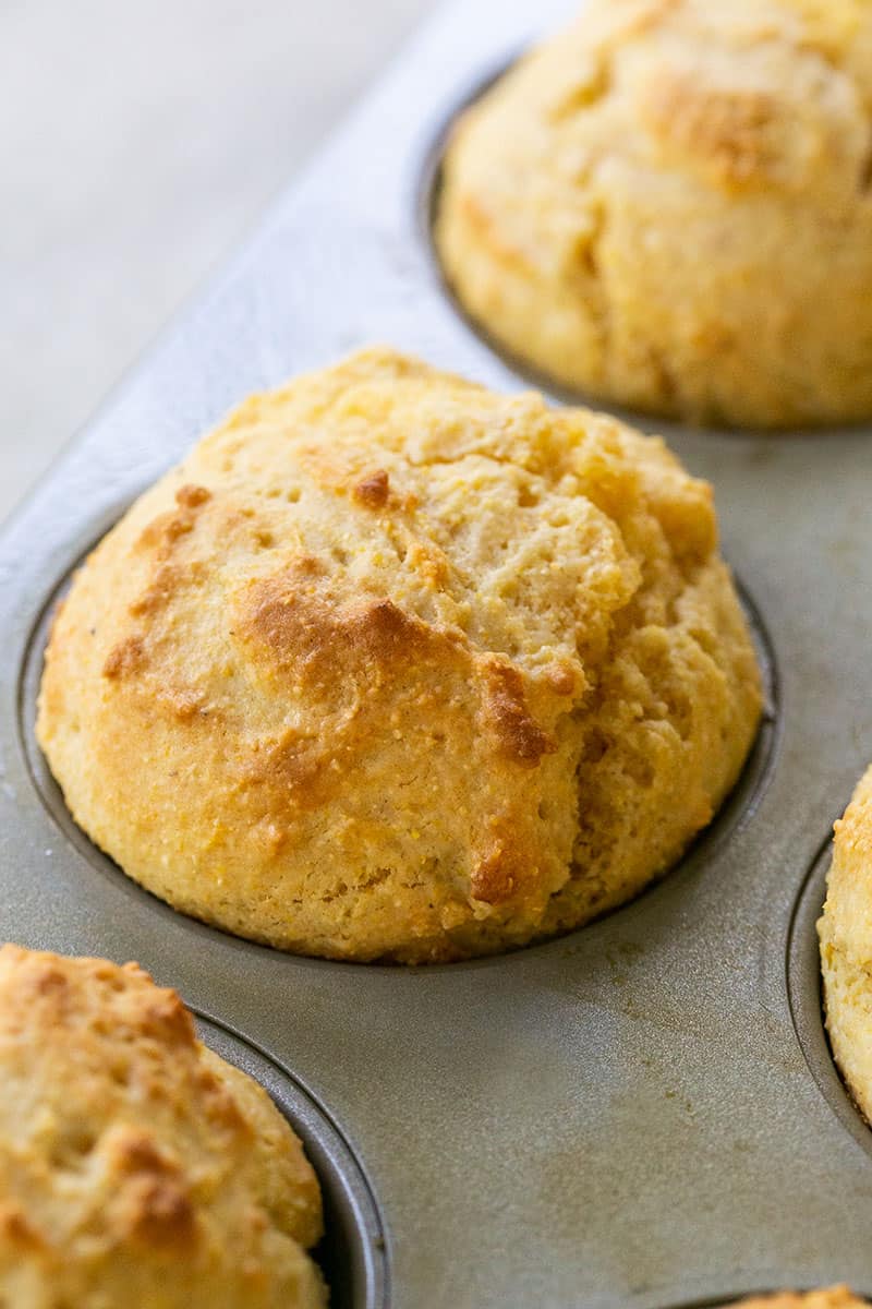 Freshly baked cornbread muffins in a muffin pan with golden, crispy tops.