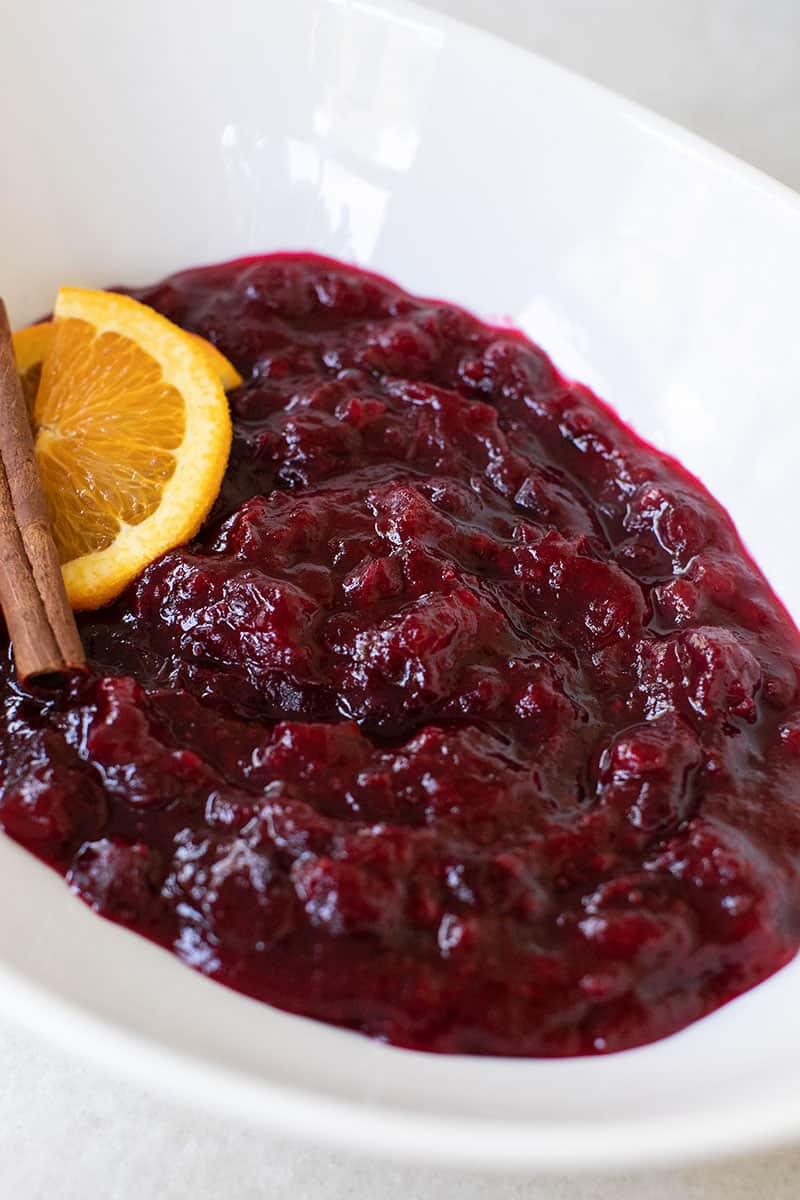 Fresh Cranberry Sauce Recipe. Served in a white bowl with oranges and cinnamon sticks. 