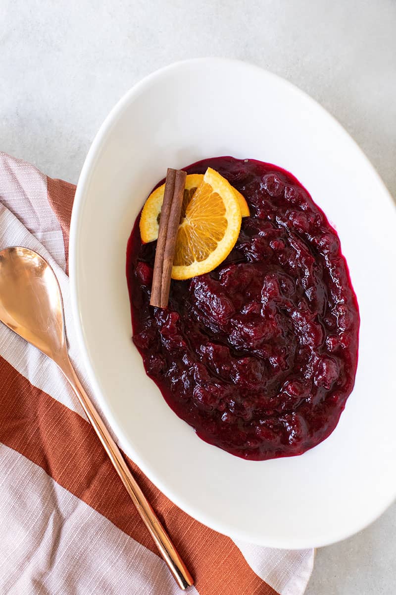homemade cranberry sauce recipe with orange and cinnamon. Served in a white bowl with garnishes and a pink towel.