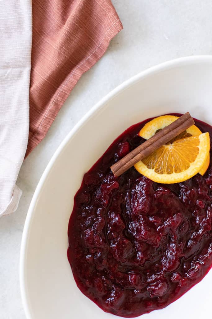 cranberry sauce served in a white bowl with orange slice and cinnamon stick.