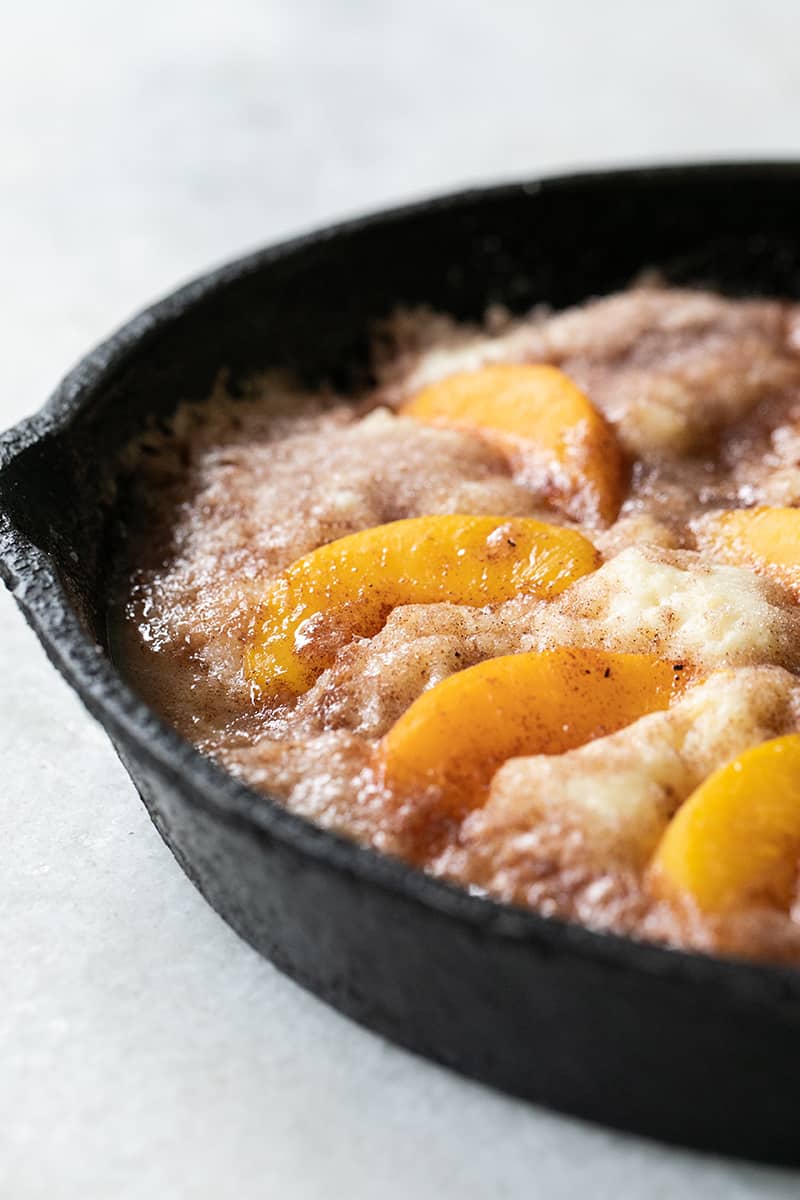 Close up photo of a peach cake with hot butter and sugar in a cast iron pan.