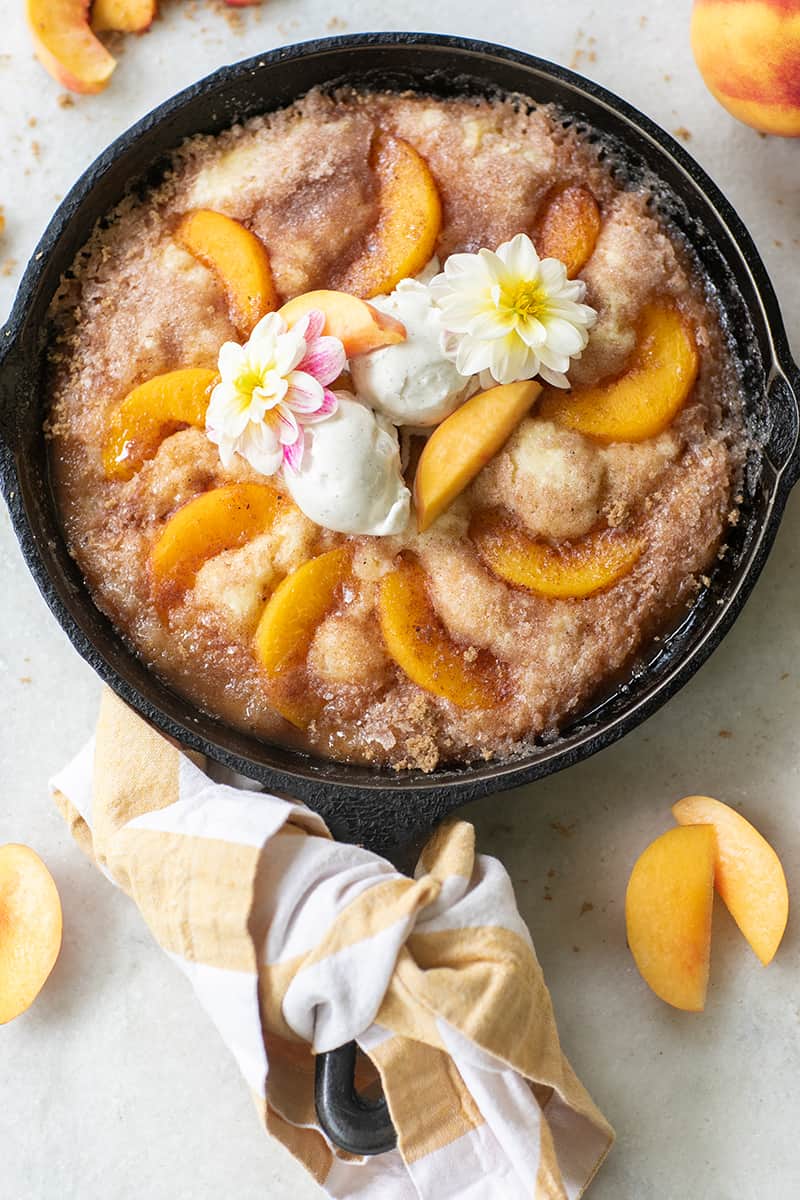 Easy peach cake recipe in cast iron skillet with ice cream and edible flowers. 
