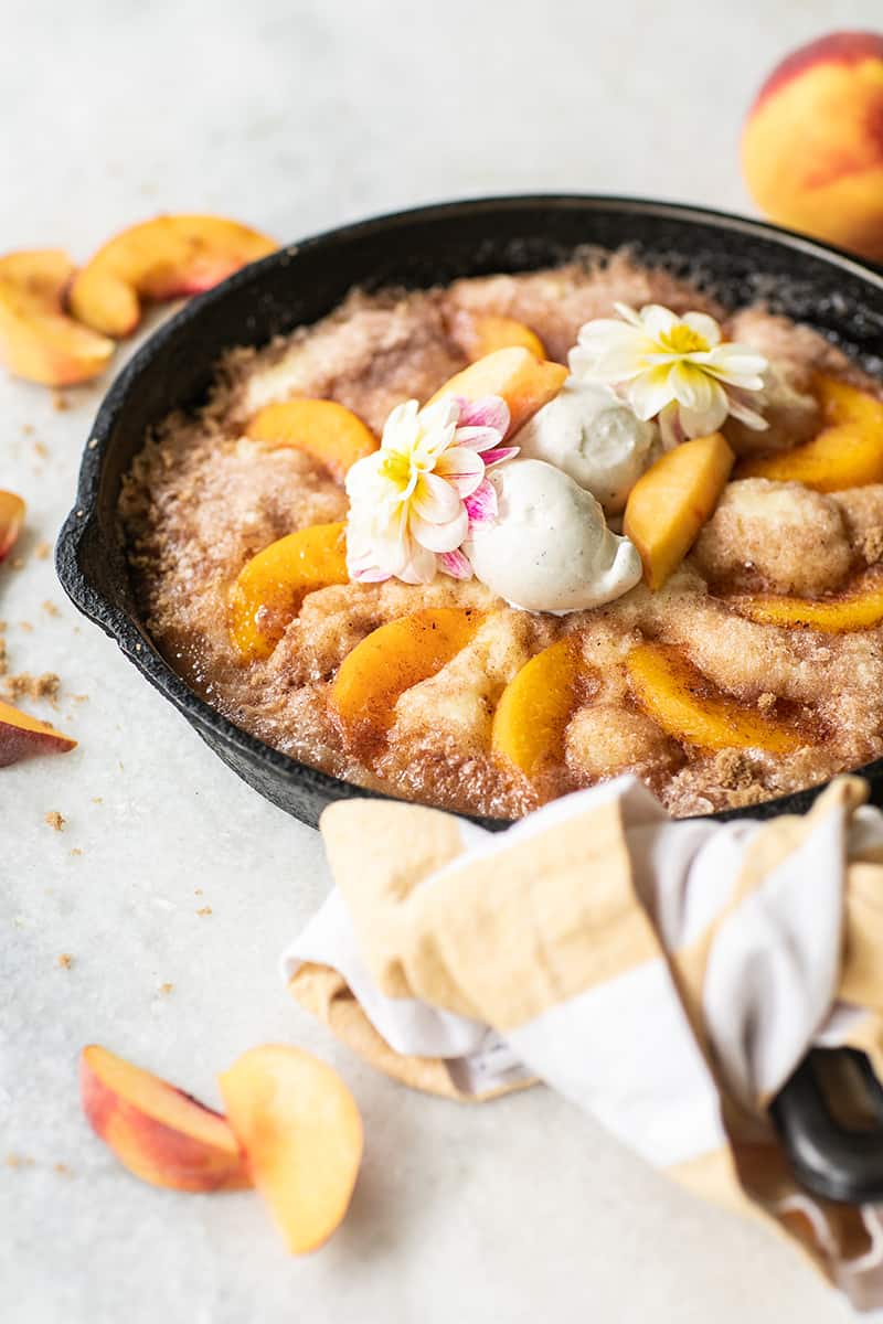 Warm and gooey peach cake in a cast iron skillet with vanilla ice cream.