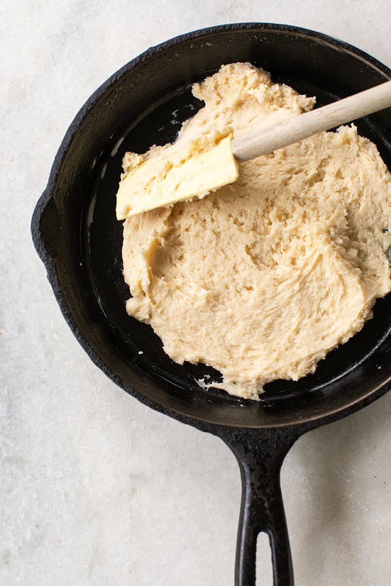 Easy peach cake batter being spread in a cast iron skillet. 