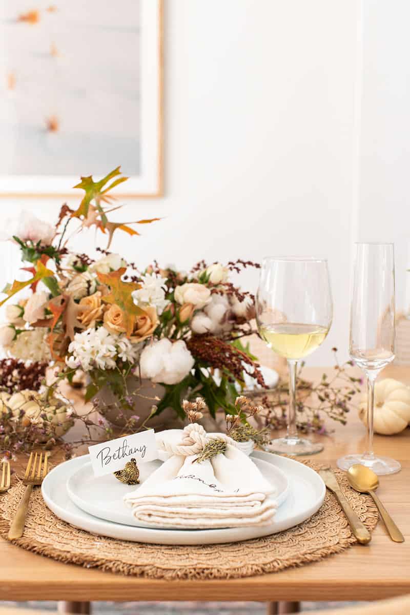 Thanksgiving table setting with flowers, white wine, white plates and napkins.