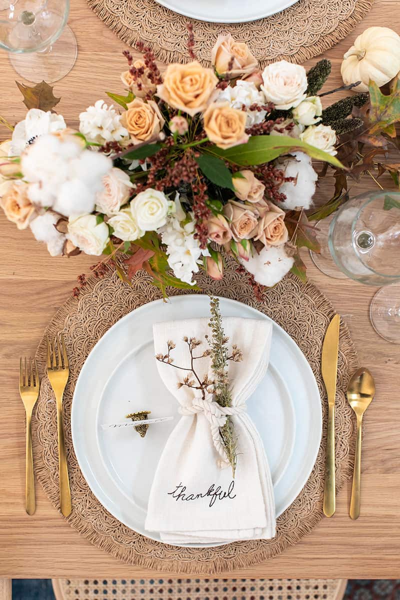 Thanksgiving table decor and table setting. White napkins, white plates, flowers, gold flatware and wine glasses.