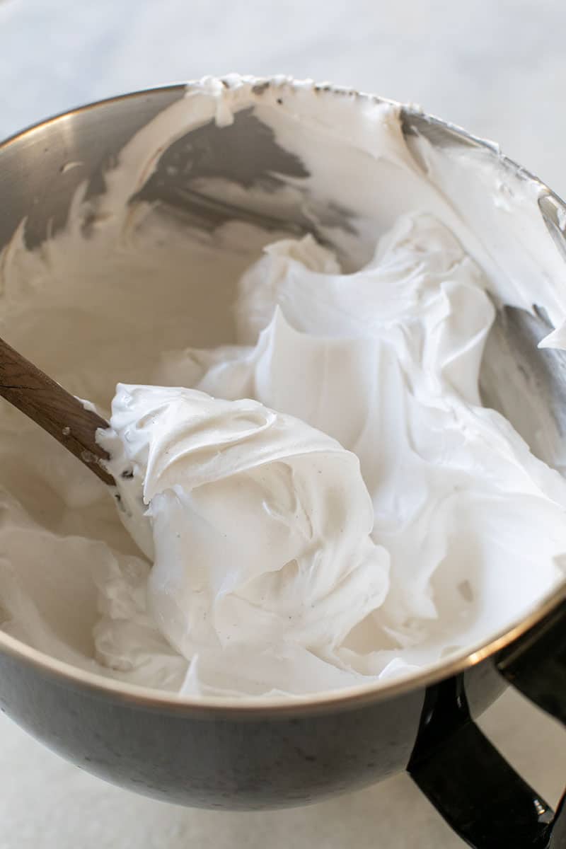 Marshmallow fluff on a wooden spoon in a metal mixing bowl. 