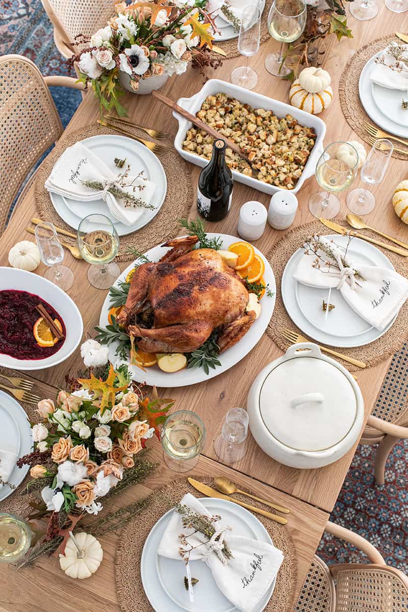 Thanksgiving table setting with a turkey, flowers, wine, wine, stuffing, cranberry sauce.