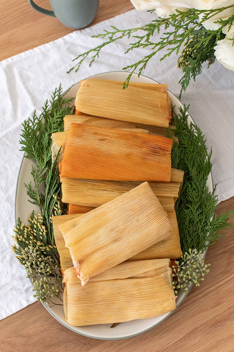 Tamales on a green and white platter with Christmas greens on the plate. - holiday dinner