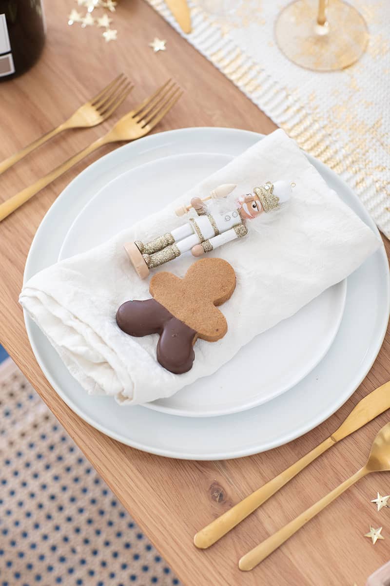 Nut cracker and gingerbread cookie on a place setting with gold flatware.