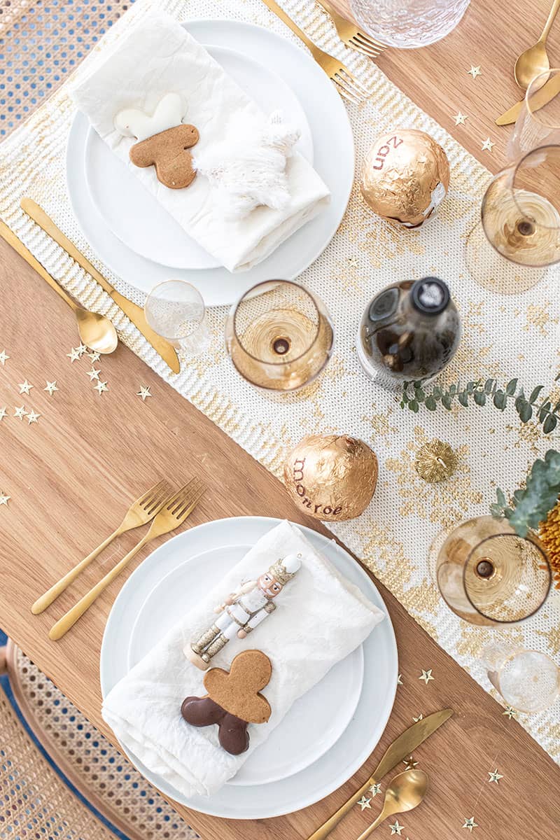 Christmas brunch table setting with gold table runner, gold stars, flowers and gingerbread cookie.