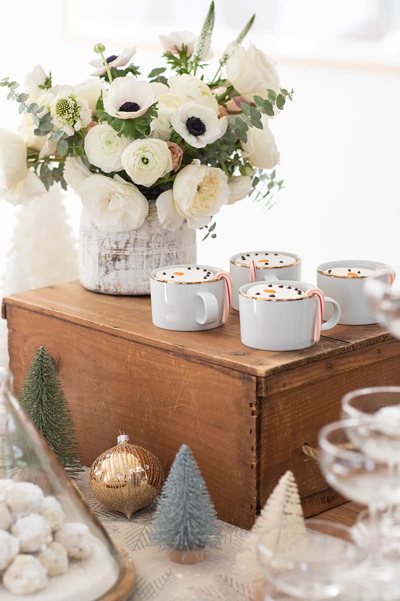 White flowers and gold cups filled with hot chocolate and snowman marshmallows. 