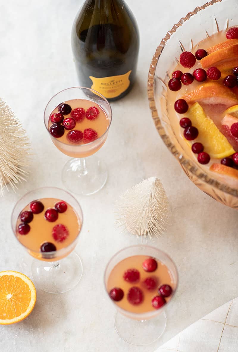 Coupe glasses filled with citrus holiday punch on a marble table with tiny white trees.