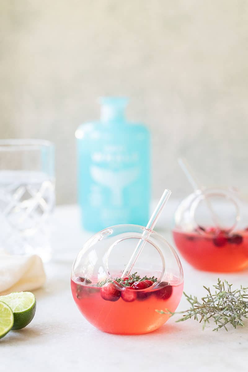 Gin and tonic is a round glass with gray whale gin and lime, cranberries and fresh thyme 