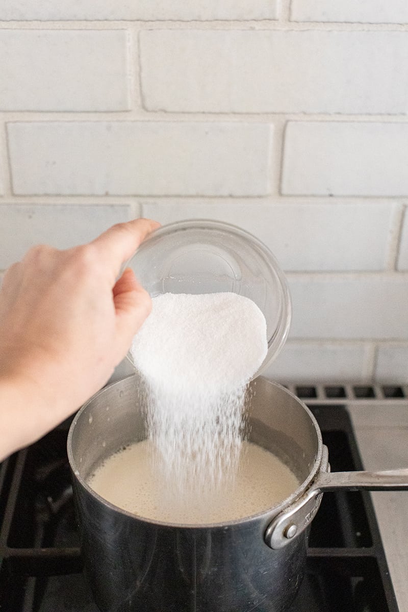 Pouring sugar into a medium sauce pan to make eggnog panna cotta 