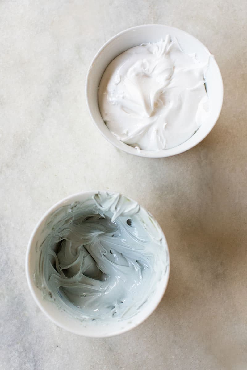 white and blue gingerbread house frosting in white bowls on a marble table. 