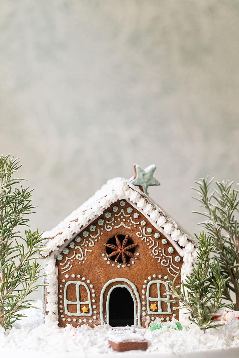 Adorable and charming gingerbread house decorated with coconut snow and rosemary trees.