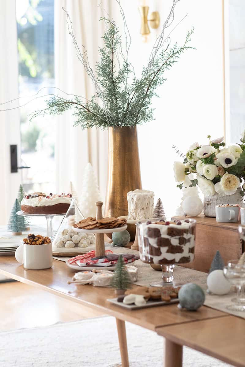 Christmas dessert table with cakes, cookies, flowers and brass vase with branches.