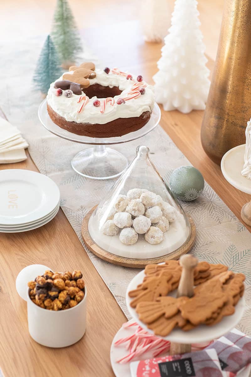 Christmas dessert table with a table runner, snowball cookies, gingerbread cake and cookies. 