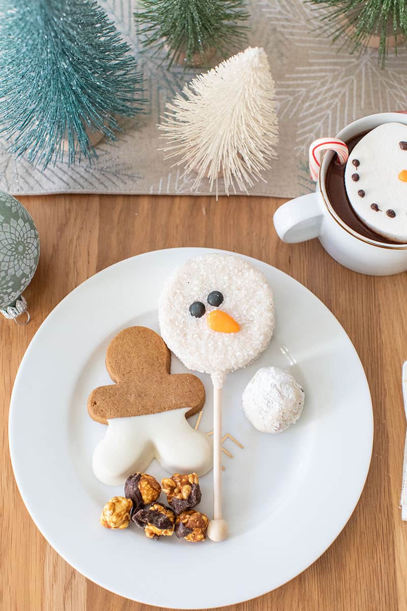 Holiday desserts on a gold and white plate. Gingerbread cookie, snowman, snowman cookie and popcorn.