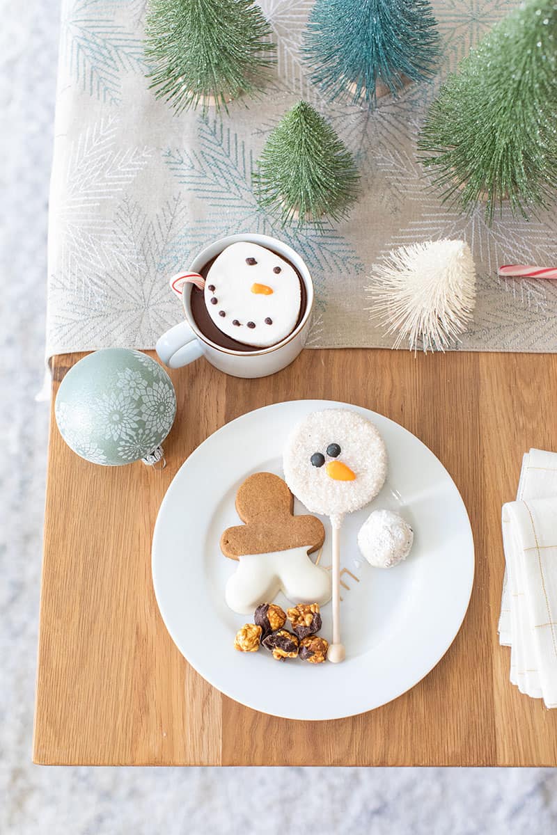 Holiday desserts on a gold and white plate with a snowman cake pop and gingerbread cookie. 